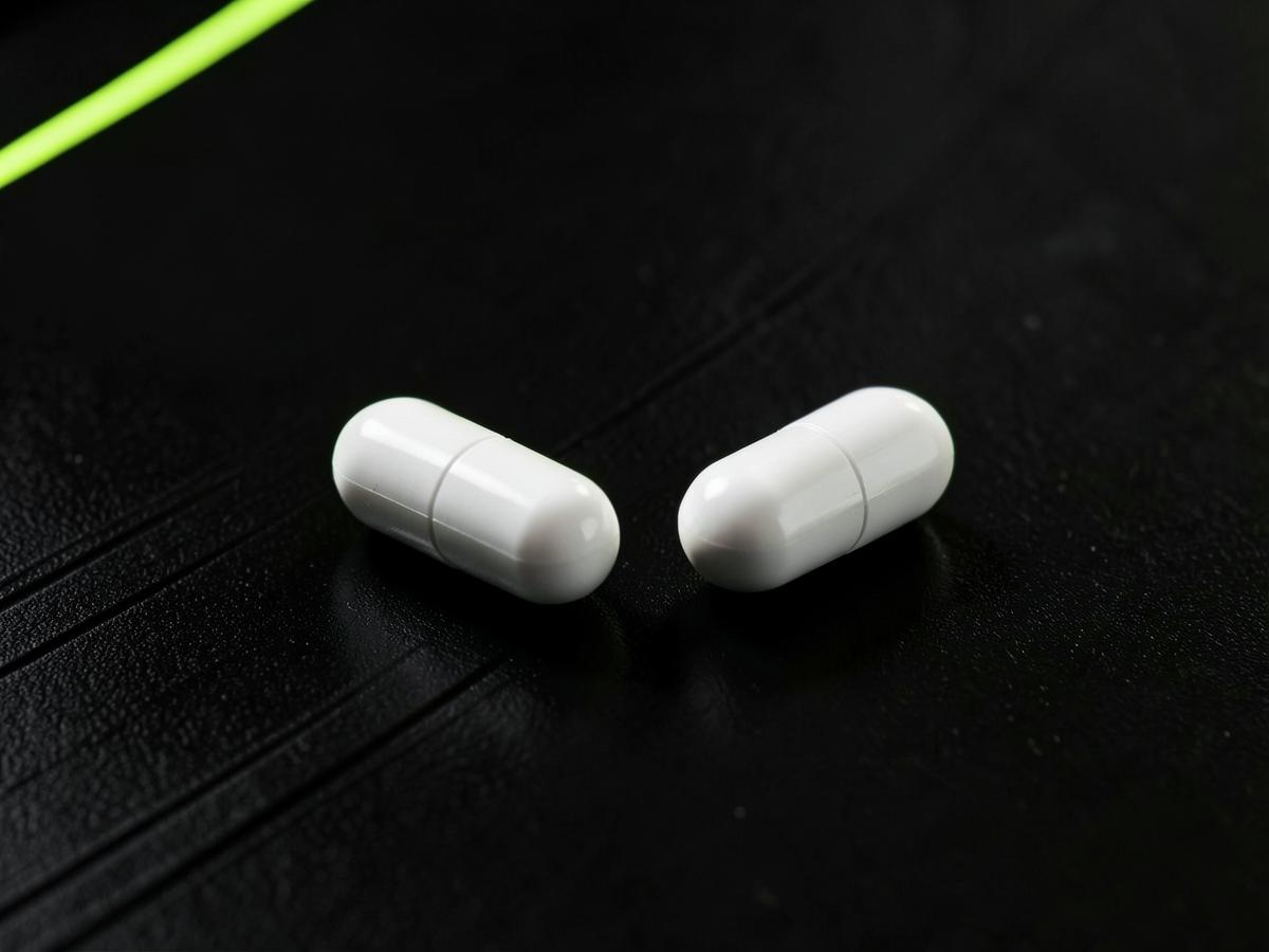 Two white supplement capsules on a dark precision surface